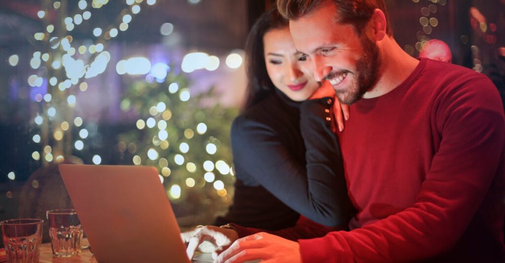 A couple using a laptop at a cozy restaurant with festive bokeh lights, enjoying online shopping together.